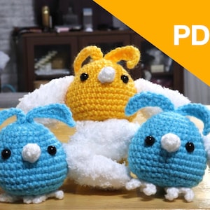Pode incluir: Três brinquedos de coelho de crochê feitos à mão em amarelo e azul, com olhos pretos e detalhes brancos. Os coelhos têm orelhas compridas e estão sentados em uma superfície branca. A imagem tem a palavra "PDF" no canto superior direito.