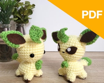 May include: Two crocheted plush toys in the shape of a Pokemon character. The toys are light yellow with green leaves and brown ears. The toys are sitting on a wooden surface.