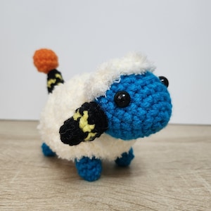 May include: A crocheted stuffed toy with a white fluffy body, blue head, black and yellow striped tail, and orange tail tip.