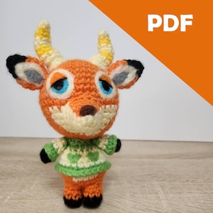 May include: Crocheted animal plush toy with orange, yellow, white, green, and black yarn. The toy is wearing a green sweater with white hearts. The toy has blue eyes and a brown nose.