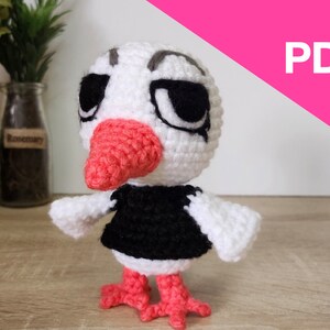 May include: Crochet amigurumi pattern of a white bird with a black shirt and orange beak and feet. The pattern is available as a PDF download.