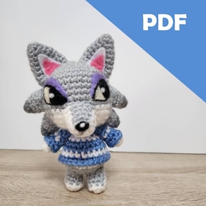 Op de afbeelding: Gehaakt grijze wolf amigurumi met een blauw-wit gestreepte trui. De wolf heeft paarse oogleden en roze oren. Het amigurumi staat op een houten oppervlak. PDF.