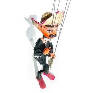 May include: A vintage puppet with a straw hat, black suit, and pink shoes. The puppet is made of wood and fabric and has a painted face.