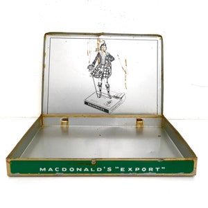 May include: An empty metal cigarette tin with a green lid. The lid has a gold trim and the words "Macdonald's "Export" printed on it. The tin has a picture of a person in a kilt on the inside of the lid.