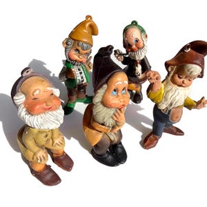 May include: A collection of five vintage garden gnome figurines. Each gnome is painted with bright colors, featuring details like pointed hats, white beards, and expressive faces. The gnomes are in various poses, adding a whimsical touch to the collection.