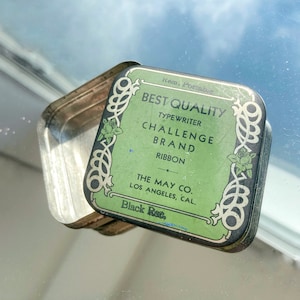 May include: A green and gold tin box with the text "Best Quality Typewriter Challenge Brand Ribbon The May Co. Los Angeles, Cal. Black Rec."  The tin box is open and the inside is silver.