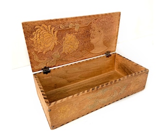 May include: A wooden box with an intricate carved design featuring a woman's face and floral motifs. The box is open, revealing the interior, which is also carved with a floral pattern.