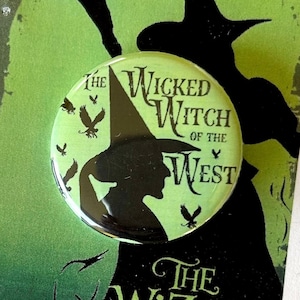 Peut inclure: Un bouton vert et noir représentant une silhouette de la Méchante Sorcière de l'Ouest du Magicien d'Oz. Le bouton porte l'inscription "The Wicked Witch of the West".
