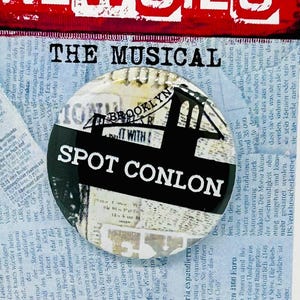May include: A poster for the musical "Newsies" with a red banner and white text. A button with the text "Spot Conlon" and a Brooklyn bridge graphic is on the poster. The background is a collage of newspaper clippings.