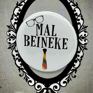May include: A button badge featuring the name "MAL BEINEKE" and a tie design, set within a decorative black frame on a grey background. The words "Addams Family THE MUSICAL" are at the bottom.
