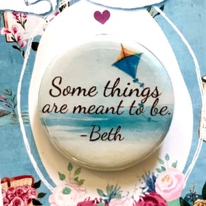 May include: A white button with a blue sky and a kite flying in the sky. The button has the quote "Some things are meant to be." - Beth. The button is on a blue background with a floral design and the words "Little Women" in a white banner.