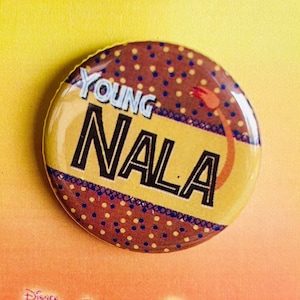 May include: A brown and yellow button with the text "Young Nala" and a brown and yellow polka dot pattern. The button is on a white card with the text "Disney The Lion King Jr."