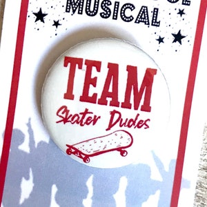 May include: White button with red text that says "Team Skater Dudes" with a black and white skateboard graphic. The button is on a white card with red text that says "High School Musical" with stars.