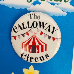 May include: A white button with a black and red circus tent design. The text "The Calloway Circus" is printed in black around the tent. The button is on a blue background with white clouds and the text "Big Fish" in green.