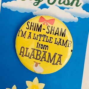 Puede incluir: Un botón amarillo con el texto "Shim-Sham I'm a little lamb from Alabama" y una pequeña ilustración de cordero blanco. El botón está sobre un fondo azul con nubes blancas y flores amarillas.