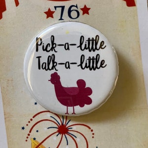 Puede incluir: Un botón blanco con una ilustración de pollo rojo y el texto "Pick-a-little Talk-a-little" sobre un fondo blanco. El botón se muestra en una tarjeta con un diseño de bandera estadounidense rojo, blanco y azul y el texto "*76* The Music Man".