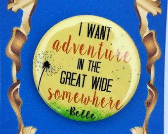 May include: A yellow button with the quote "I want adventure in the great wide somewhere - Belle" from the movie Beauty and the Beast. The button is on a blue background with a gold frame.