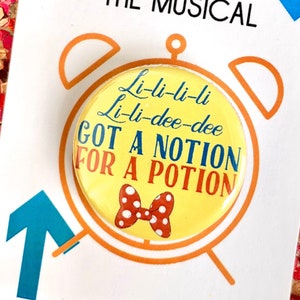 May include: A yellow and white button with a red bow and the text "Li-li-li-li Li-li-dee-dee GOT A NOTION FOR A POTION" on it. The button is on a white card with the text "9TO5 THE MUSICAL" on it.