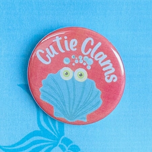 May include: A pink button with the text "Cutie Clams" and a cartoon clam with googly eyes. The button is on a blue background with the text "Disney's The Little Mermaid" in white.