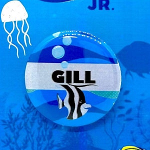 May include: A blue and white button with the words "Finding Nemo Jr." and "Gill" on it. The button features a cartoon fish with black and white stripes.