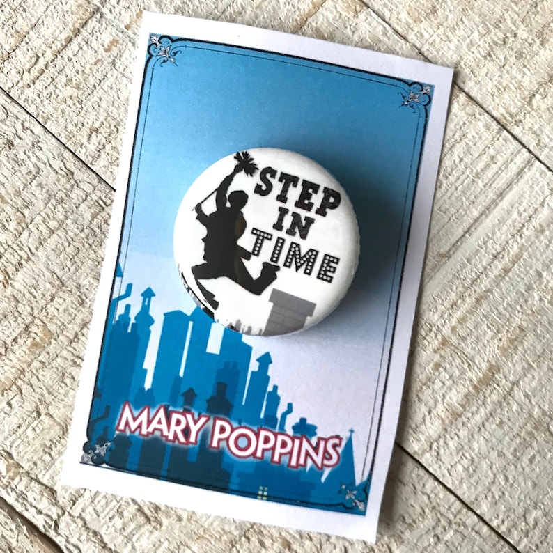 K&ouml;nnte beinhalten: Ein wei&szlig;er Knopf mit einer schwarzen Silhouette eines Schornsteinfegers, der in die Luft springt. Der Knopf tr&auml;gt den Text "Step in Time" in schwarzer Schrift. Der Knopf befindet sich auf einer Karte mit blauem Hintergrund und dem Text "Mary Poppins" in wei&szlig;.