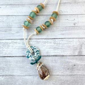 May include: A white rope necklace with teal and brown beads, a teal and white fabric circle, and a brown seashell pendant.