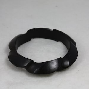 May include: A black wooden bangle with a wavy, organic design. The bangle is smooth and polished.