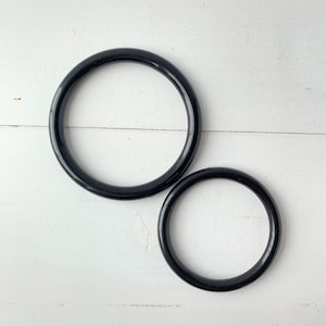 Puede incluir: Dos anillos de plástico negro de diferentes tamaños. El anillo más grande tiene un diámetro de aproximadamente 15 cm y el anillo más pequeño tiene un diámetro de aproximadamente 10 cm.