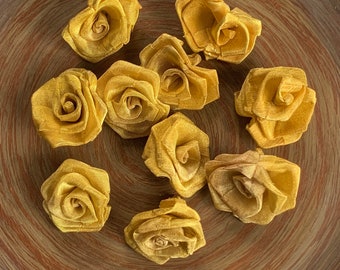Puede incluir: Diez pequeñas flores de rosa de tela de color amarillo dorado. Las rosas están hechas de satén y tienen una textura ligeramente arrugada.