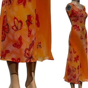 Peut inclure: Robe longue orange avec un imprimé papillon. La robe présente une encolure dégagée et une jupe fluide. Les papillons sont rouges et noirs, et la robe est en tissu léger. La robe est présentée sur un mannequin.