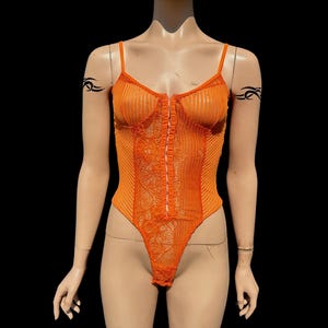 Peut inclure: Combinaison en dentelle orange avec une fermeture éclair sur le devant. La combinaison a une texture côtelée et une silhouette ajustée.