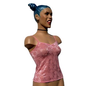 Puede incluir: Busto de maniquí con cabello azul recogido en un moño. El maniquí lleva una camiseta sin mangas rosa de encaje floral y un collar negro. El maniquí tiene la lengua fuera.