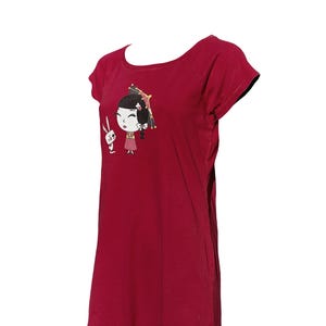 Può includere: T-shirt bordeaux con un'illustrazione a cartoni animati di una ragazza e un coniglio. La ragazza ha i capelli neri e indossa un vestito rosa. Il coniglio è bianco. La t-shirt ha maniche corte e scollo tondo.