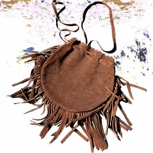 Peut inclure: Un sac en daim marron avec une bordure en franges et une longue bandoulière. Le sac est fermé par un cordon.