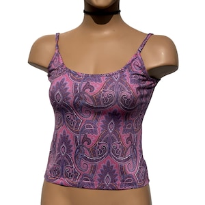 May include: A pink and purple paisley print vest top with thin straps. The top is displayed on a mannequin. The paisley pattern features a mix of pink, purple, and brown hues. The vest top has a scoop neckline.