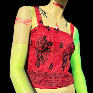 Puede incluir: Un top corto rojo y negro con estampado floral y cuello fruncido. El top está hecho de una tela suave y elástica y tiene un corte holgado.