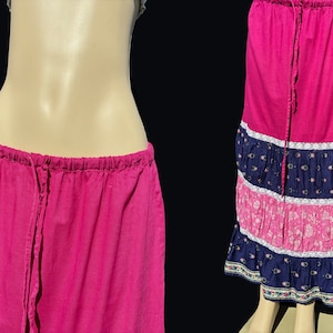 Op de afbeelding: Een lange roze rok met een witte kantversiering en een blauwe en roze bloemenprint. De rok heeft een trekkoord.