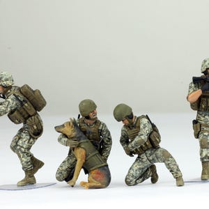 May include: Miniature figurines of soldiers in camouflage uniforms, some kneeling, and one with a German Shepherd dog. The soldiers are armed with rifles and machine guns, and wear helmets and tactical gear. The figures are on clear plastic bases.