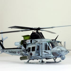 Puede incluir: Un modelo de helicóptero militar gris y blanco con palas negras y el texto "US MARINES" y "06" en el lateral.