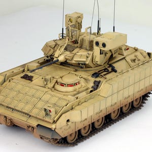 Könnte beinhalten: Ein tanfarbenes militärisches Panzerfahrzeug mit einem Turm und einer Kanone. Das Fahrzeug hat ein Tarnmuster und steht auf weißem Hintergrund.