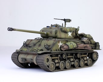May include: A green military tank model with a camouflage pattern and a star on the side. The tank has a long barrel and is covered in canvas bags and other equipment.