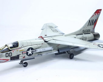 May include: A white and gray model airplane with red accents. The plane has a star on the side and the text "US NAVY" on the tail. The tail also has the text "NM 150326".