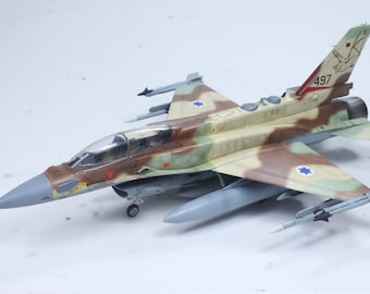 May include: A detailed model of an Israeli Air Force F-16 fighter jet, painted in desert camouflage with the Israeli flag on the wings and tail. The model has a clear canopy, a detailed cockpit, and a variety of weapons and equipment.
