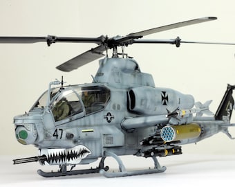 May include: A detailed model of a military helicopter, painted in shades of gray with black accents. The helicopter features a shark mouth design on the front, a rotating main rotor, and various mounted weapons. The number "47" is visible on the side.