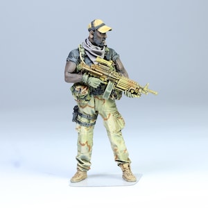 May include: A military action figure wearing a camouflage uniform and a tan hat, holding a black and gold machine gun.