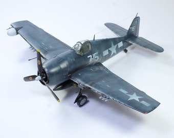 May include: A model of a blue and gray Grumman F6F Hellcat fighter plane with a white star on the tail and wings. The plane has a yellow propeller and the number "715" on the side.