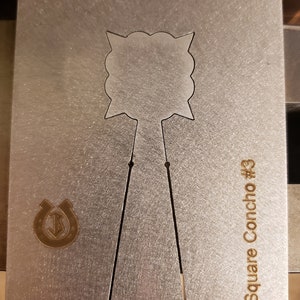 Puede incluir: Una tarjeta de concho de metal plateado con un dise&ntilde;o recortado. La tarjeta tiene un agujero en la parte superior y el texto "1" Square Concho #3" y "This Side Up". Tambi&eacute;n es visible un logotipo de herradura.