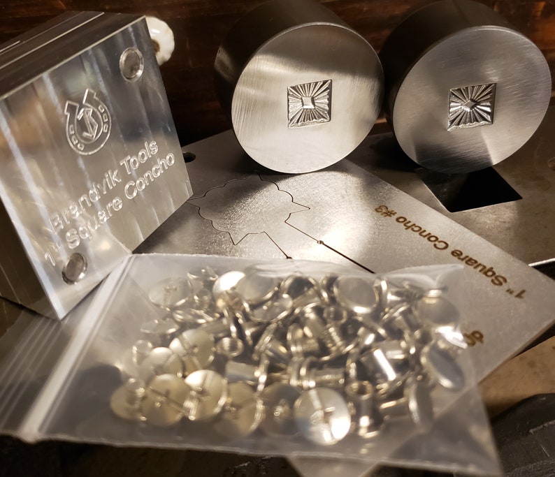 Puede incluir: Una colecci&oacute;n de herramientas y hardware para trabajar metales. La imagen presenta un bloque de metal cuadrado con el texto "Brendvik Tools 1" Square Concho", dos sellos de metal circulares con un dise&ntilde;o de sol cuadrado y una bolsa de conchos plateados.