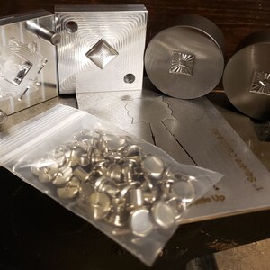 Puede incluir: Una colecci&oacute;n de herramientas y hardware de metal. La imagen muestra varios sellos met&aacute;licos cuadrados y circulares con dise&ntilde;os geom&eacute;tricos detallados, junto con una bolsa de pl&aacute;stico transparente llena de peque&ntilde;os sujetadores met&aacute;licos. Tambi&eacute;n es visible una plantilla de metal.