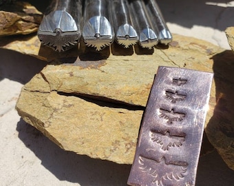 May include: Five metal stamps with eagle designs are displayed, with a metal plate showing stamped eagle impressions. The stamps are in a row, each with a different sized eagle. The plate shows the stamped impressions.
